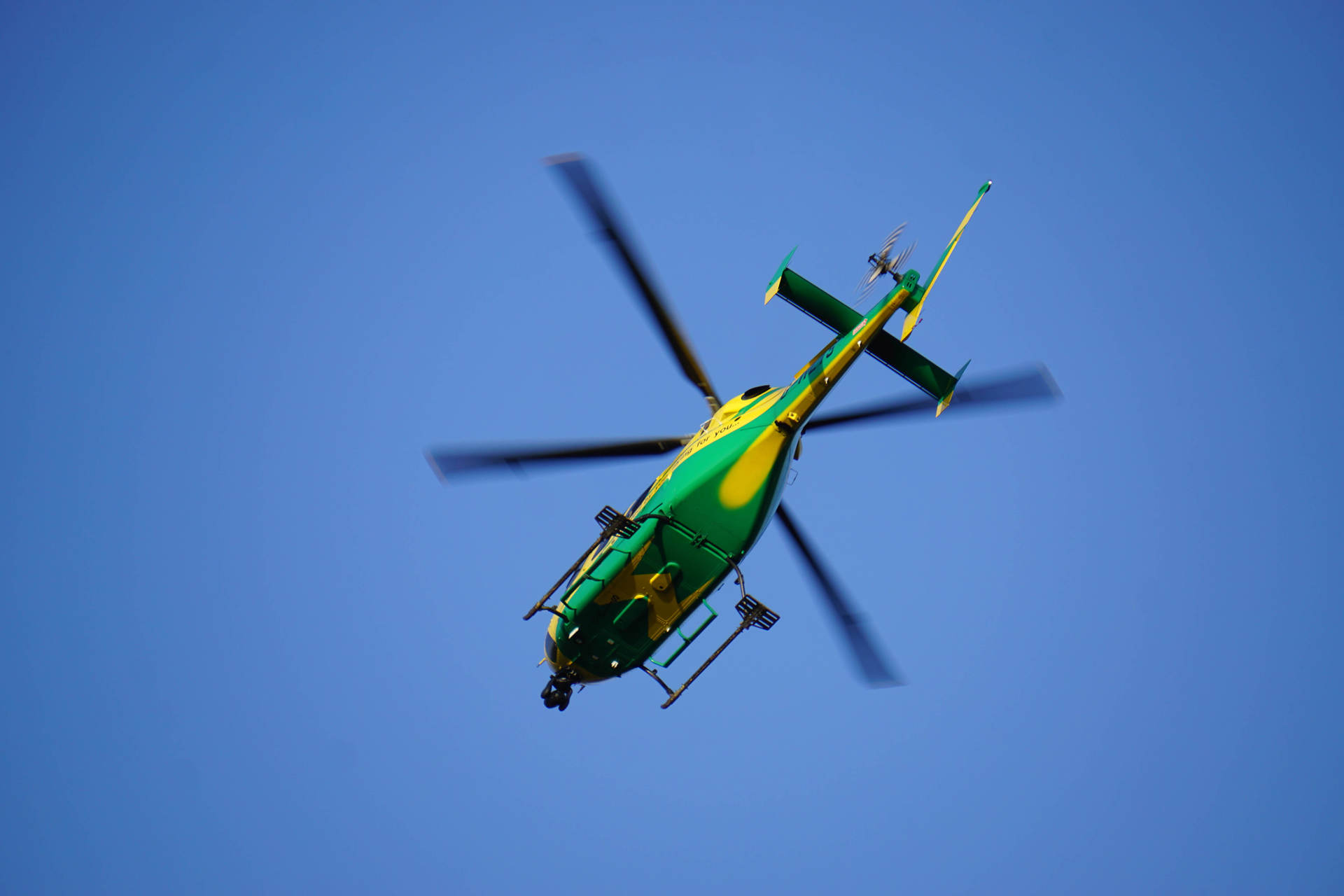 The yellow and green helicopter in flight against a blue sky.