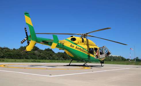 The yellow and green helicopter landed on the helipad against a blue sky.