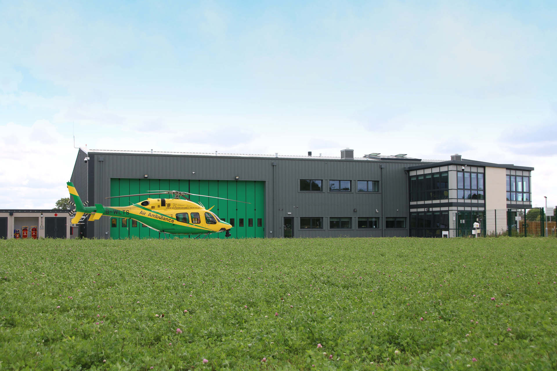 A panoramic view of the Wiltshire Air Ambulance helipad and airbase featuring the yellow and green Bell-429 helicopter on its helipad.