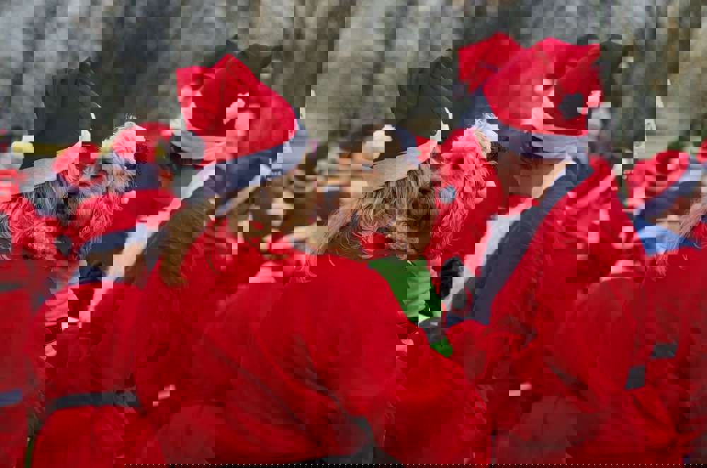 A group of people wearing red Santa suits, with one holding a dog dressed as an elf