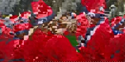 A group of people wearing red Santa suits, with one holding a dog dressed as an elf A group of people wearing red Santa suits, with one holding a dog dressed as an elf