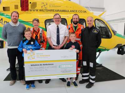 A group of visitors in front of the helicopter holding a large cheque inside the hanger