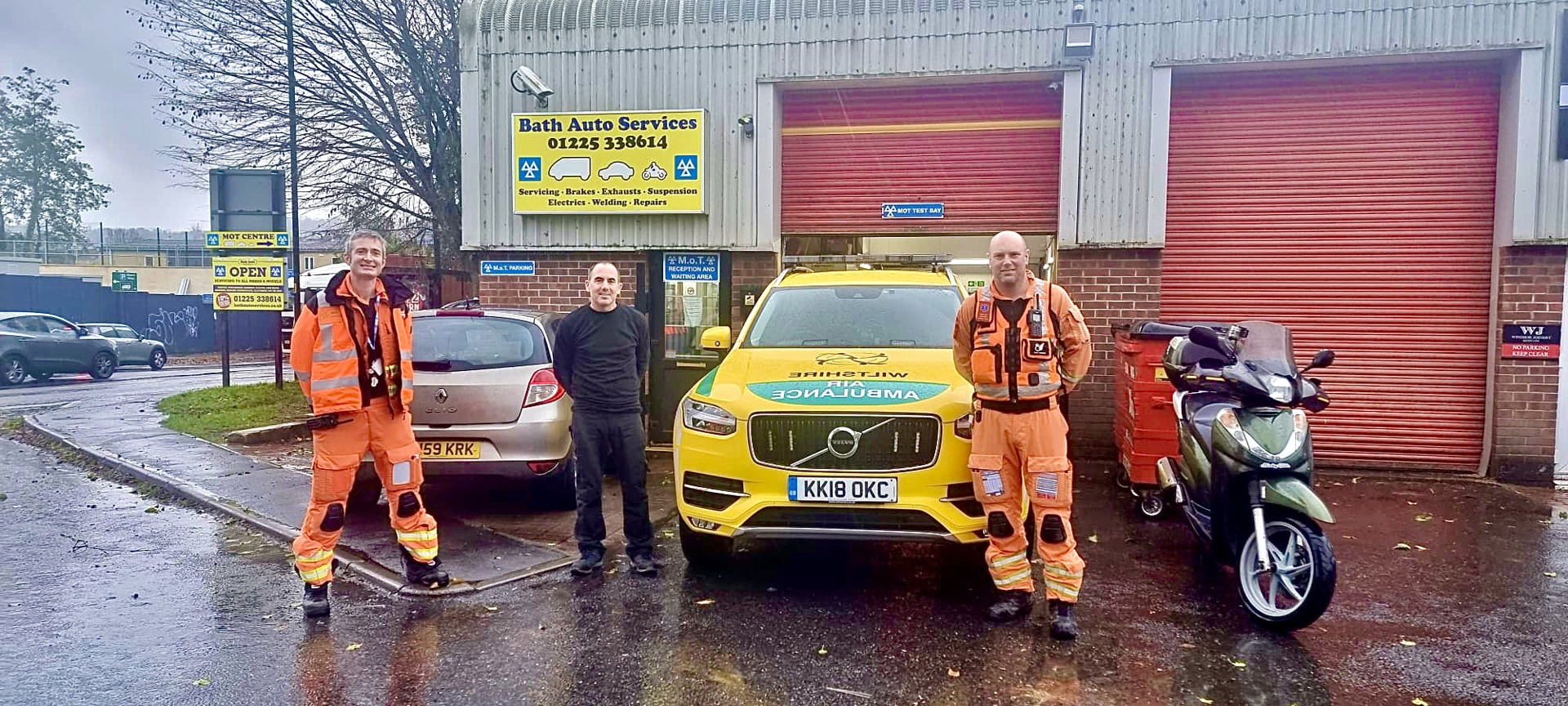 Critical care doctor Reuben and paramedic Dan wearing orange flight suits, standing in front of Bath Autos with a mechanic and Wiltshire Air Ambulance's critical care car Critical care doctor Reuben and paramedic Dan wearing orange flight suits, standing in front of Bath Autos with a mechanic and Wiltshire Air Ambulance's critical care car