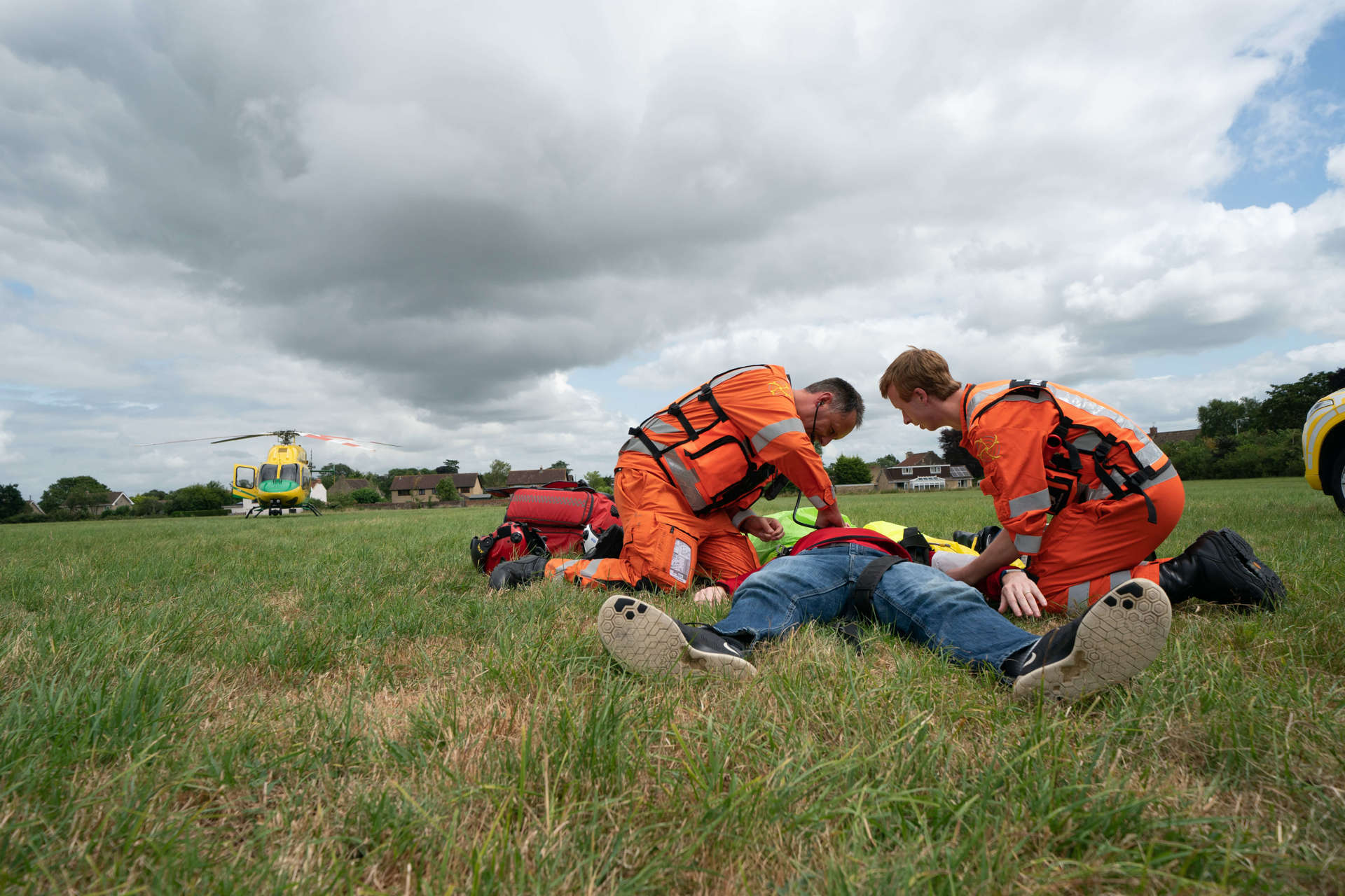 A staged incident in a field with two paramedics and a patient with the helicopter in the background.