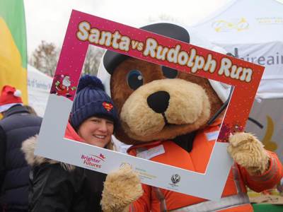 Bear mascot Wilber holding a red and white Santa vs Rudolph run selfie frame with supporter Bear mascot Wilber holding a red and white Santa vs Rudolph run selfie frame with supporter