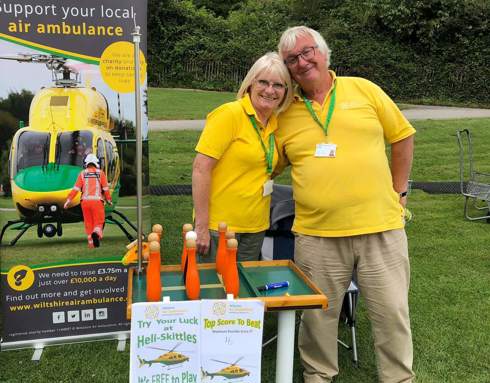 Two volunteers stood in front of a Wiltshire Air Ambulance banner at an event.