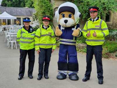 Marsha the teddy bear pilot mascot stood in a courtyard with three police officers wearing high-vis jackets. Marsha the teddy bear pilot mascot stood in a courtyard with three police officers wearing high-vis jackets.