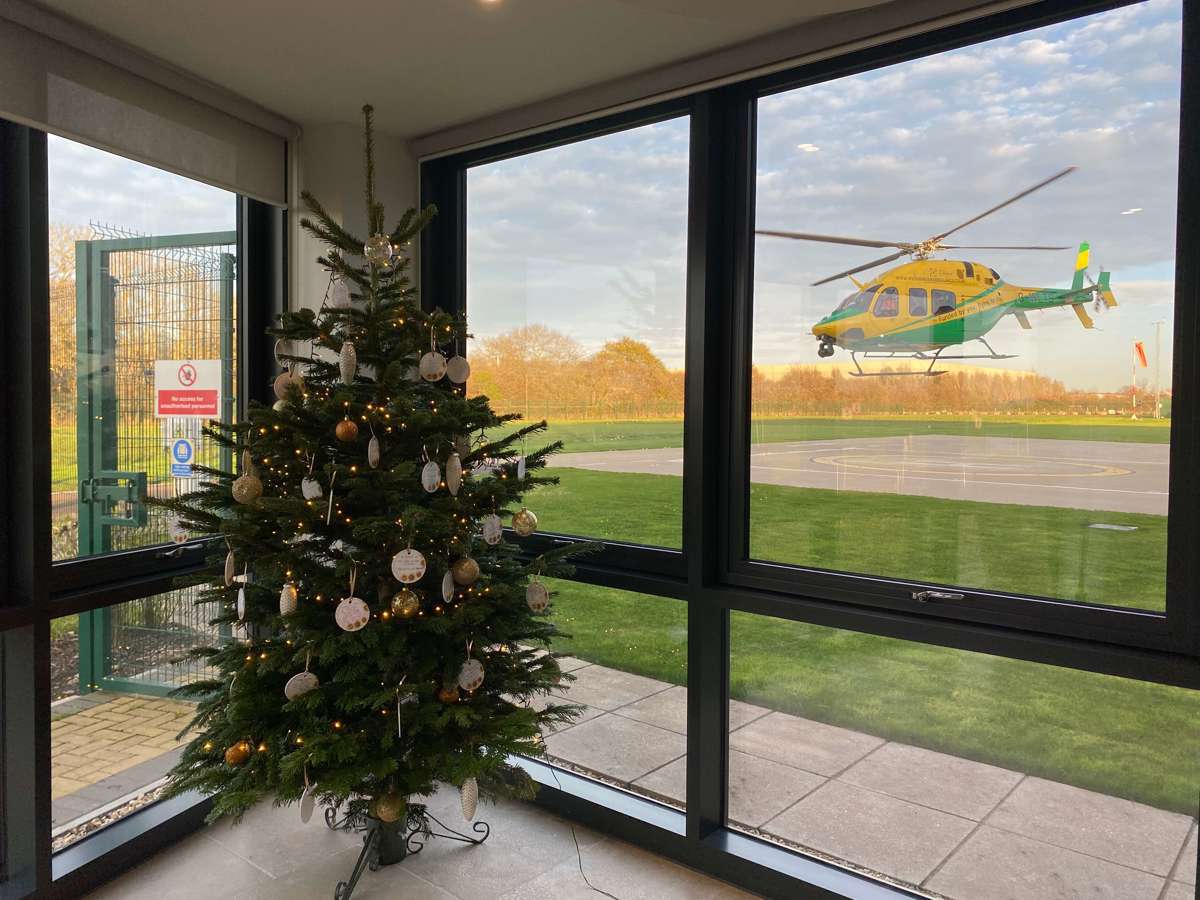 A Christmas tree decorated in gold baubles located in the airbase reception with the helicopter landing in the background.