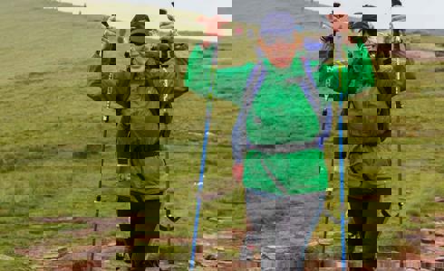 A person wearing a green raincoat and blue backpack, holding walking poles in the air