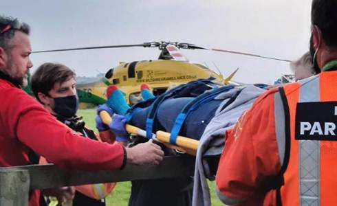 A patient being carried over a fence on a stretcher. The Bell 429 helicopter is in the background.