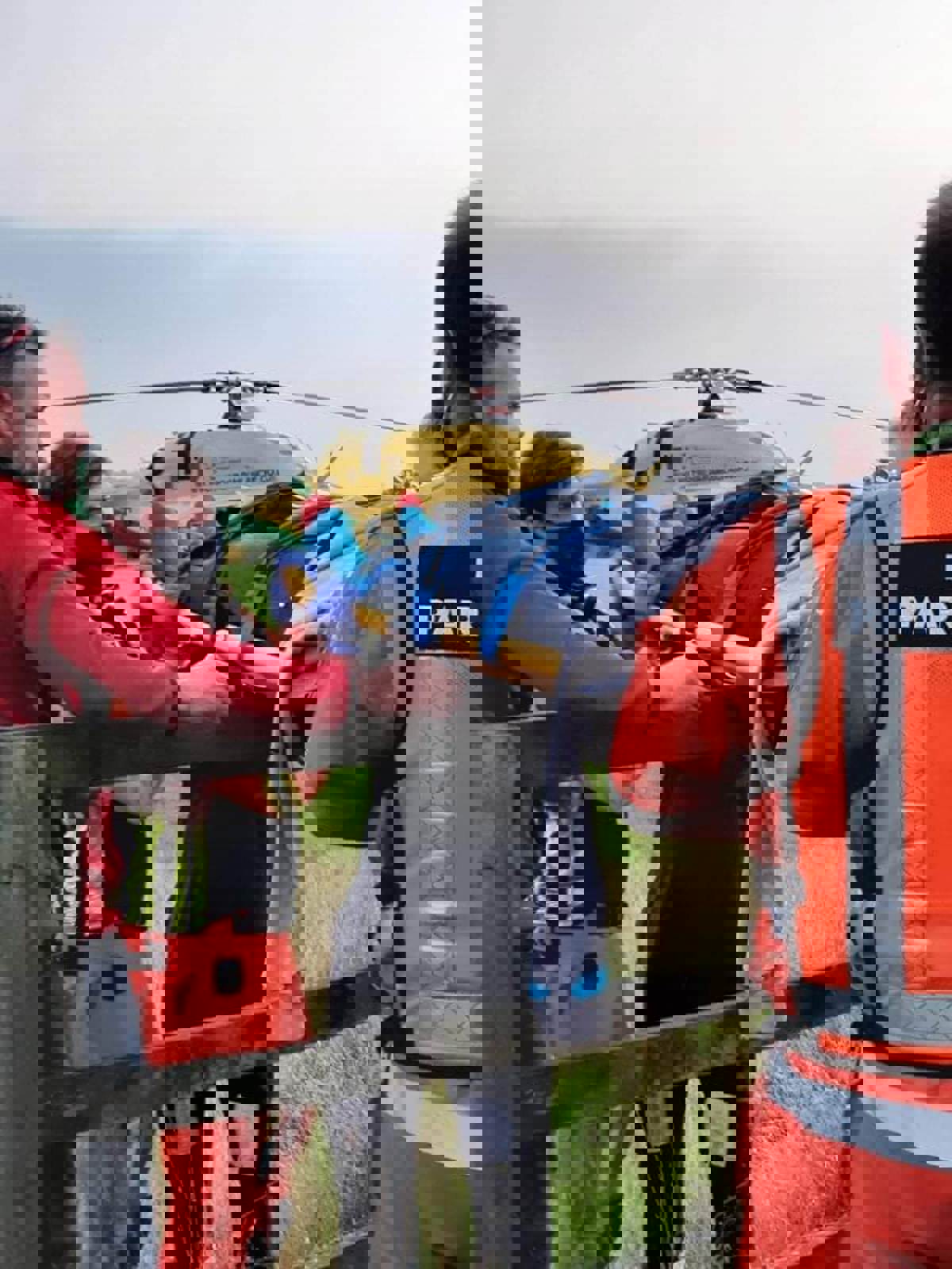 A patient being carried over a fence on a stretcher. The Bell 429 helicopter is in the background. A patient being carried over a fence on a stretcher. The Bell 429 helicopter is in the background.