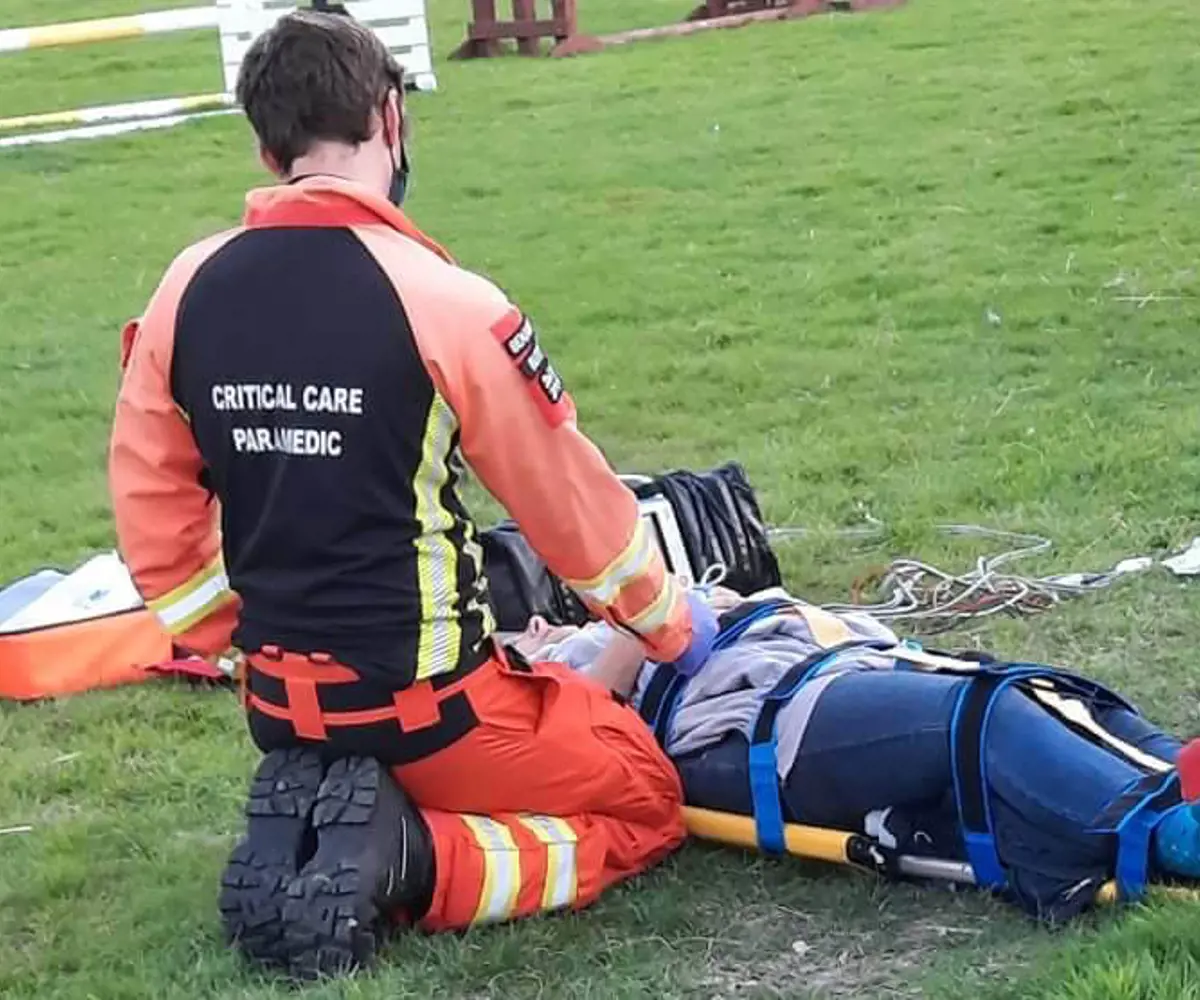A patient laying on a stretcher with a critical care paramedic knelt by their side