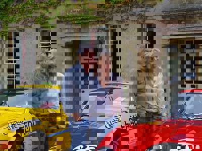A photo of Nick and Annette Mason in front of the Middlewick House and two sports cars. A photo of Nick and Annette Mason in front of the Middlewick House and two sports cars.