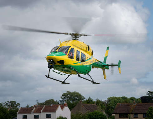 A yellow and green Bell-429 helicopter coming in to land in a field.