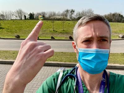 Dr Reuben Cooper at Southmead Hospital helipad pointing at the Wiltshire Air Ambulance helicopter on the helipad.