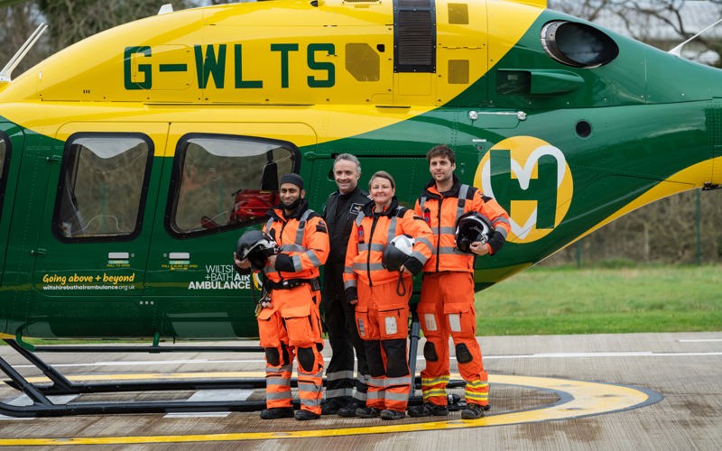 A group of air ambulance colleagues standing in front of a yellow and green helicopter