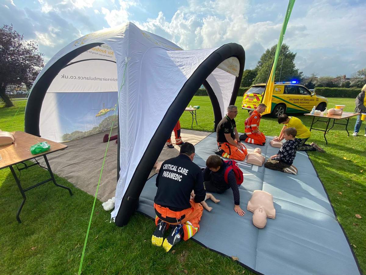 Three paramedics delivering Emergency Awareness Training in a blow up gazebo with members of the public using mannequins.