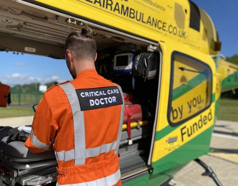 A doctor wearing an orange flight suit restocking a kit bag in the back of the Wiltshire Air Ambulance helicopter.