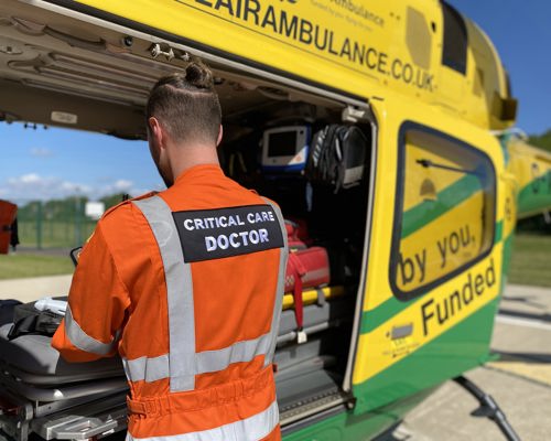 A doctor wearing an orange flight suit restocking a kit bag in the back of the Wiltshire Air Ambulance helicopter.