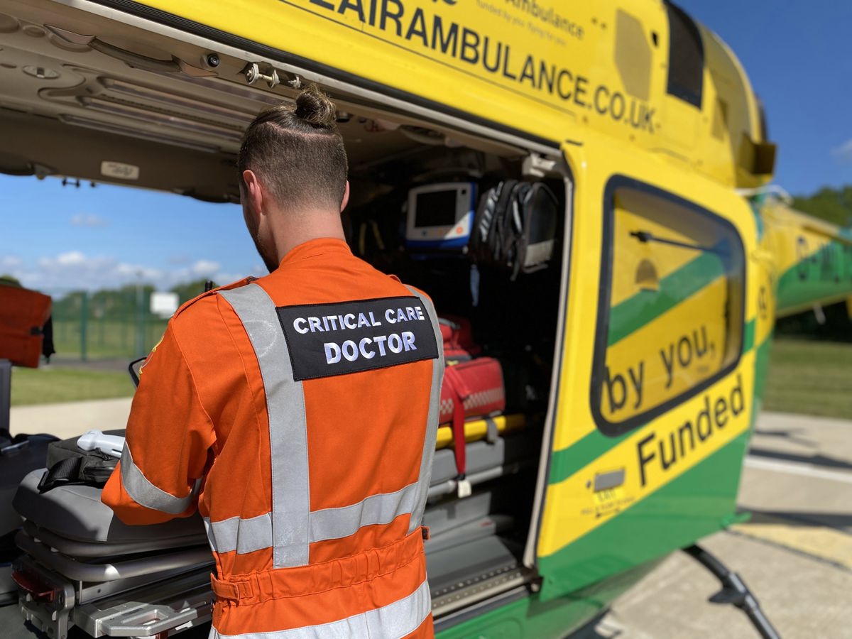 A doctor wearing an orange flight suit restocking a kit bag in the back of the Wiltshire Air Ambulance helicopter.