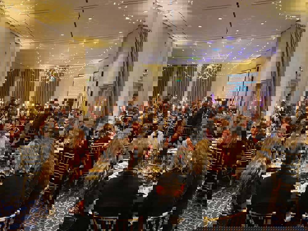 Black and gold themed charity ball. Groups of people wearing smart clothing, sitting on gold chairs around round tables