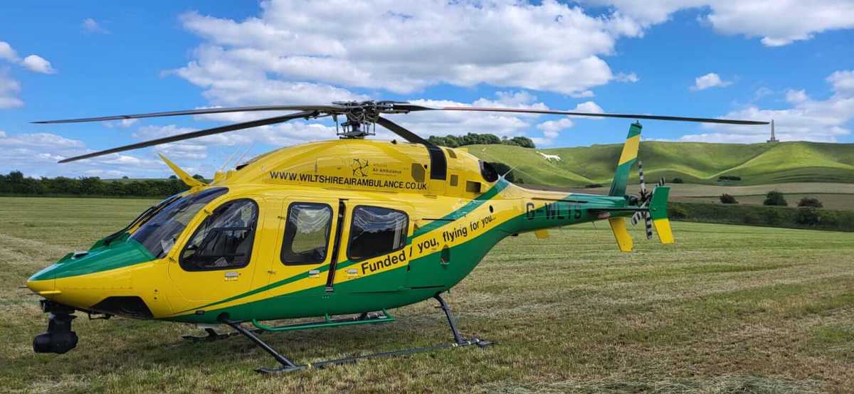 Yellow and green Wiltshire Air Ambulance helicopter landed in a field with white horse in the background