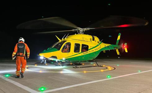 A paramedic wearing an orange flight suit walking towards a yellow and green helicopter