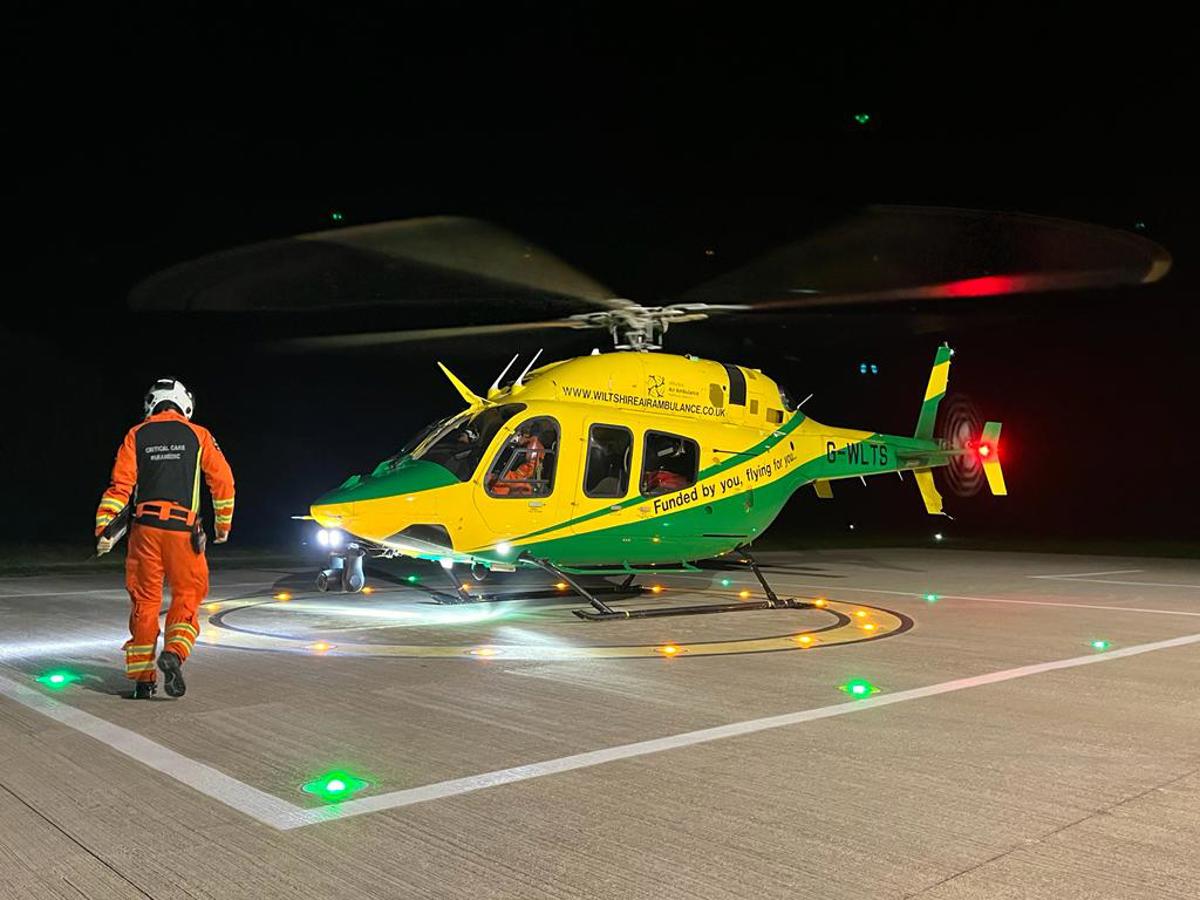 A paramedic wearing an orange flight suit walking towards a yellow and green helicopter