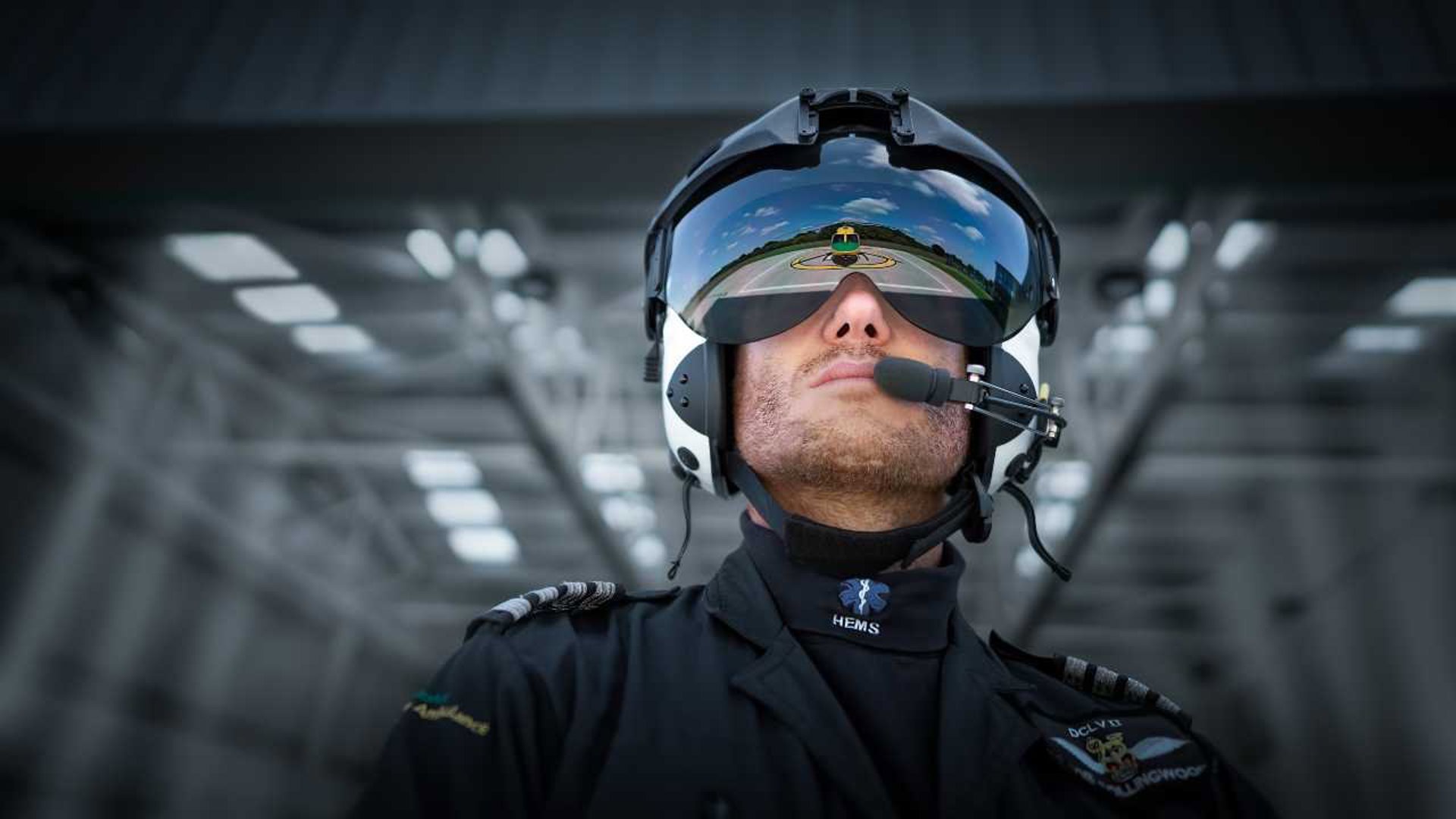 Pilot Rob Collingwood looking at the helicopter whilst wearing a flight helmet and visor. There is a reflection of the helicopter in the visor. Pilot Rob Collingwood looking at the helicopter whilst wearing a flight helmet and visor. There is a reflection of the helicopter in the visor.
