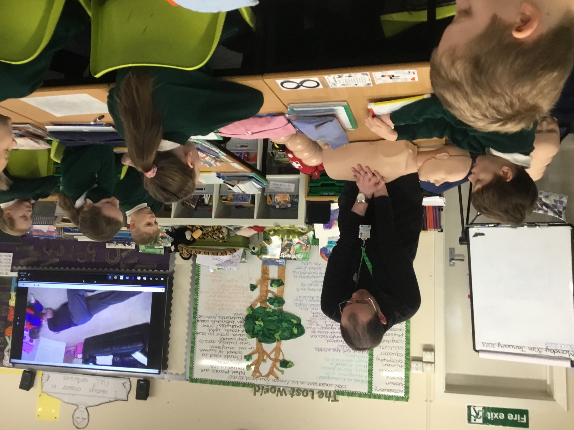 A man performing CPR on a manikin, with school children watching on