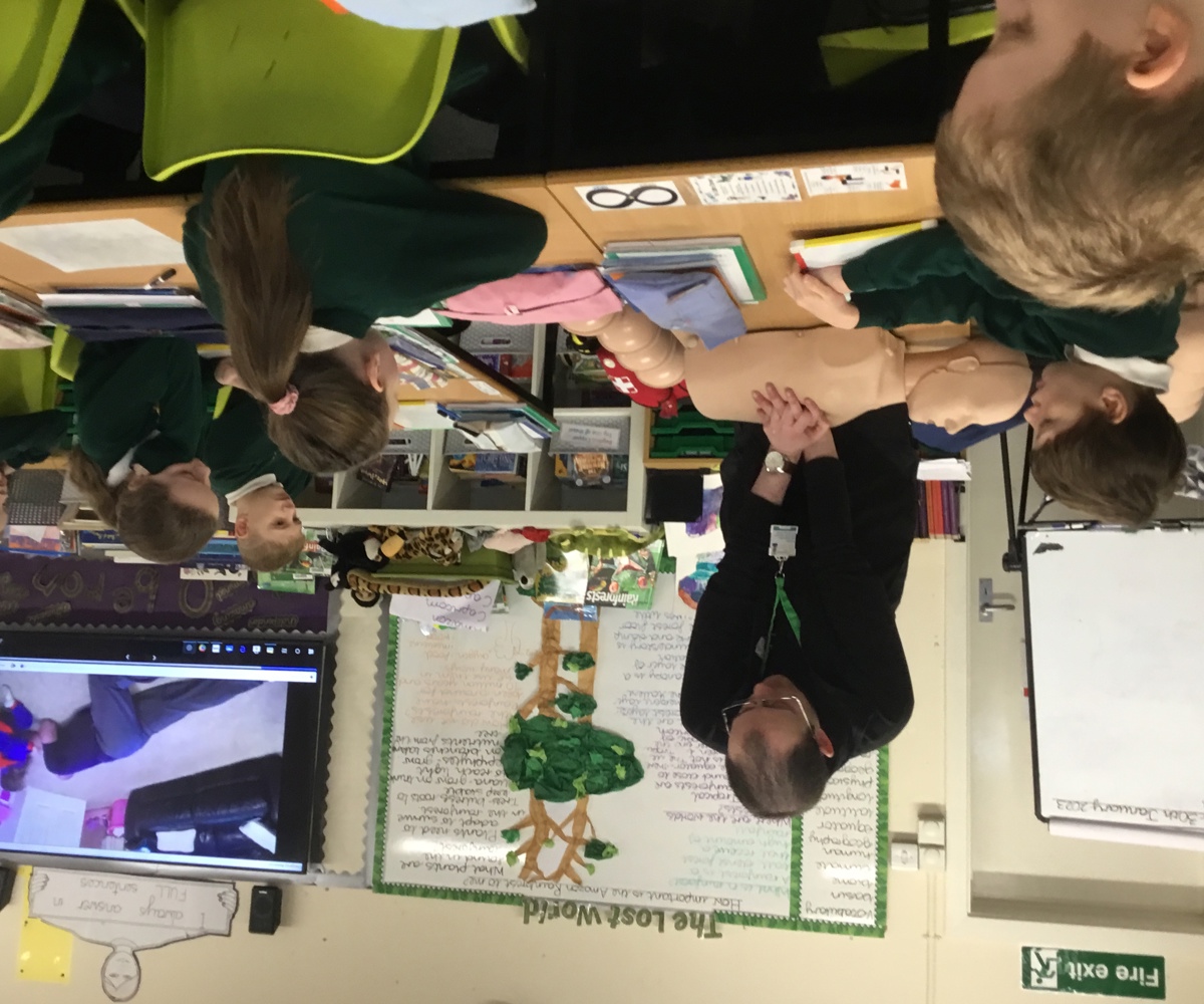 A man performing CPR on a manikin, with school children watching on