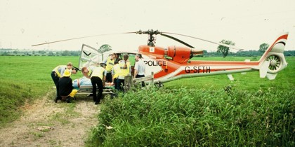 A scanned photo of a red helicopter landed in a field with police lifting a patient on a stretcher. A scanned photo of a red helicopter landed in a field with police lifting a patient on a stretcher.