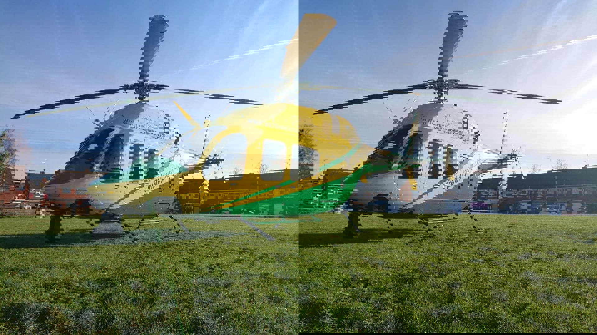 A yellow and green helicopter landed on a green in Swindon, with houses behind A yellow and green helicopter landed on a green in Swindon, with houses behind