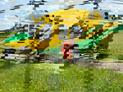 A photo of a paramedic and pilot smiling at the camera whilst perching on the step of the Wiltshire Air Ambulance's yellow and green helicopter