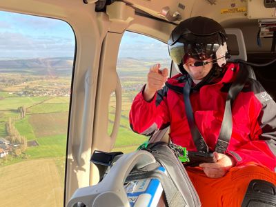 A photo of a doctor wearing a flight helmet pointing at the camera, whilst in flight