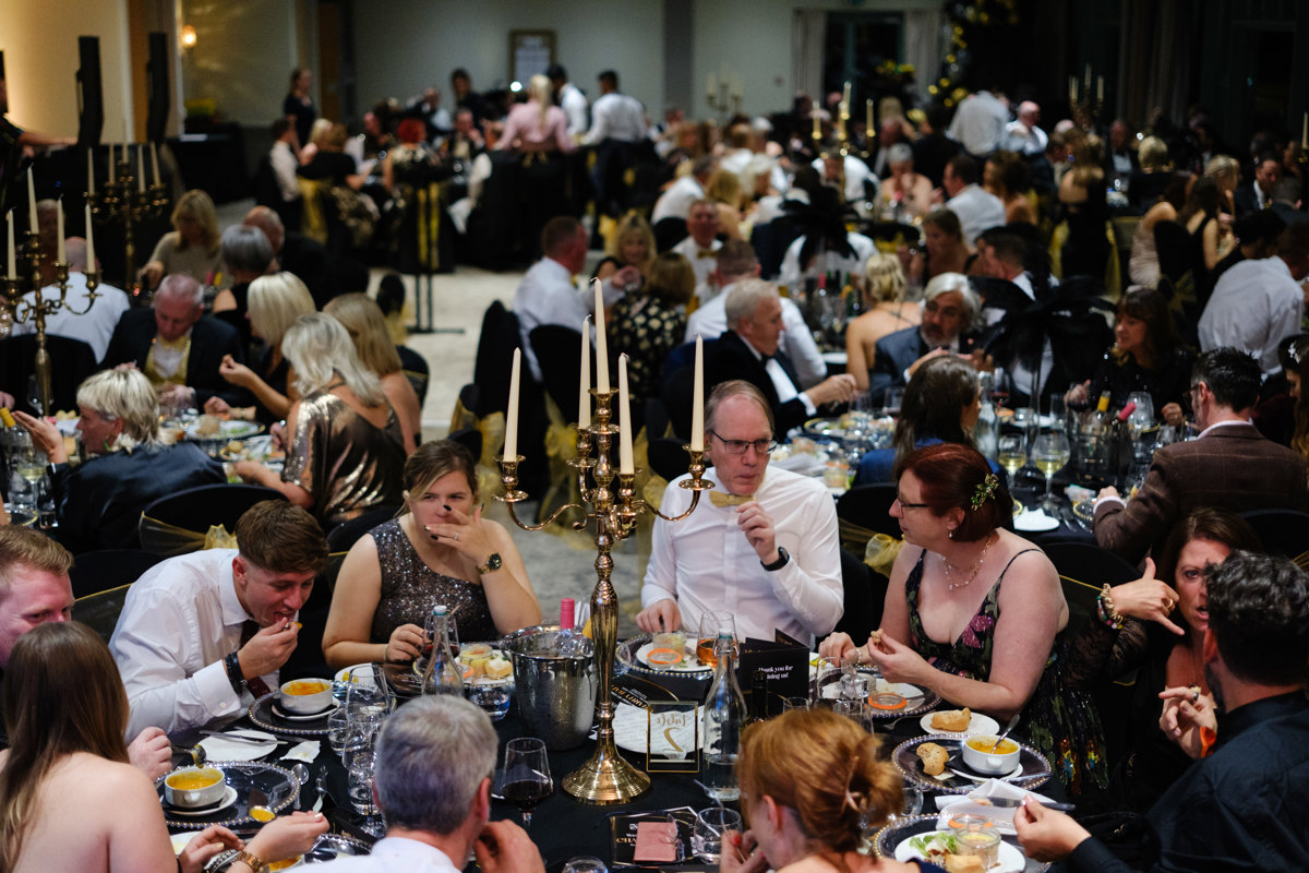 A group of people sitting around tables wearing black and gold