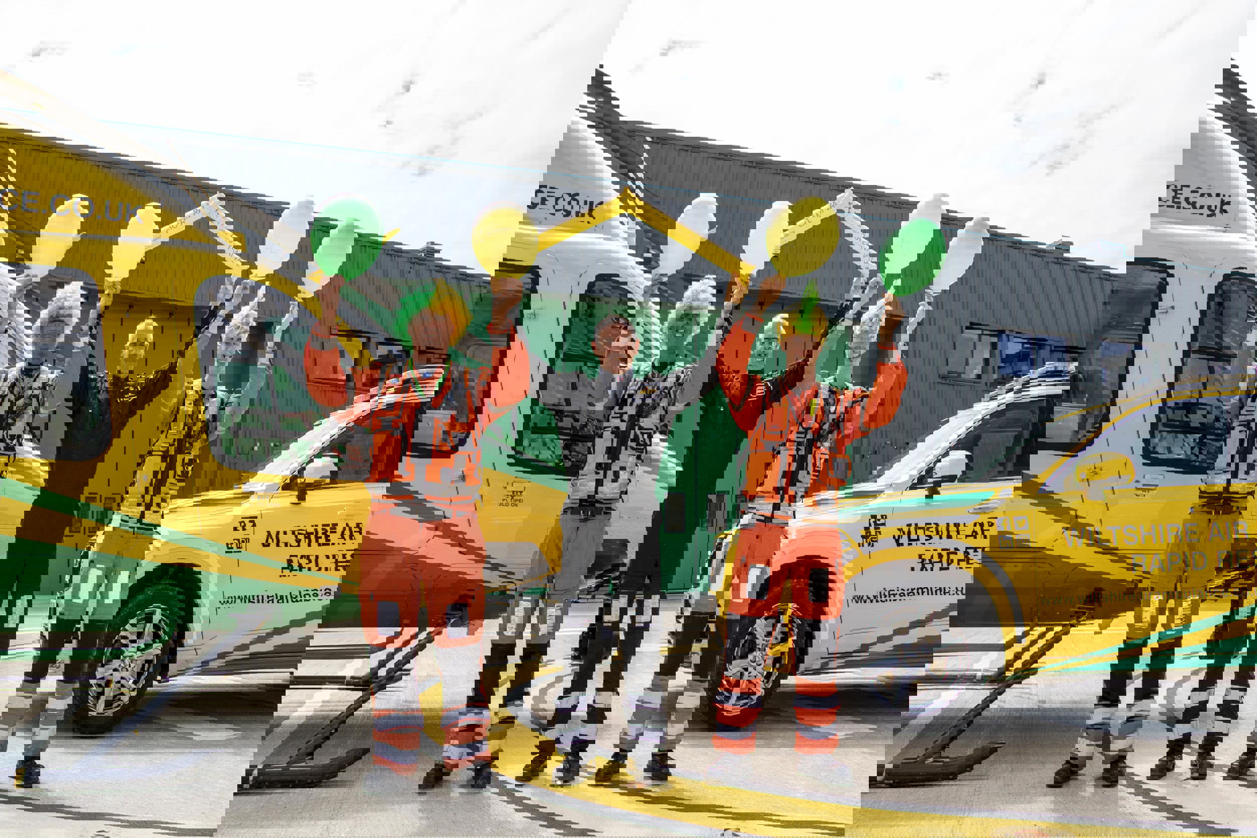 Paramedic Rich Miller wearing a yellow and green curly wig and holding yellow and green balloons, Rob Backus holding yellow Team WAA cheer sticks and Craig Wilkins wearing a yellow and green mohawk wig and holding yellow and green balloons