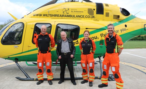 Patient Martyn Dormer standing in front of the helicopter with critical care paramedics Dan and Sophie, and doctor Reuben who are wearing orange flight suits,