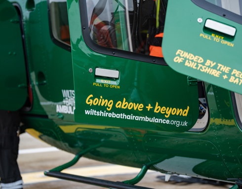 Yellow text with going above + beyond and funded by the people of wiltshire + bath on the doors of a green helicopter