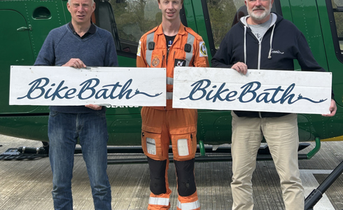Three men holding Bike Bath banners in front of a yellow and green helicopter
