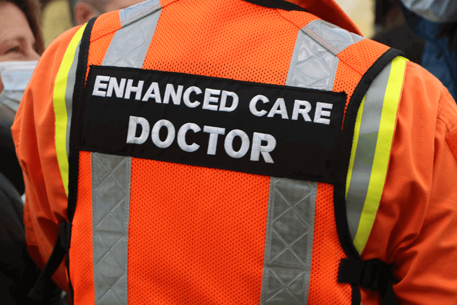 A close up of a person's back wearing and orange flight suit and vest with 'enhanced care doctor' written on the back A close up of a person's back wearing and orange flight suit and vest with 'enhanced care doctor' written on the back