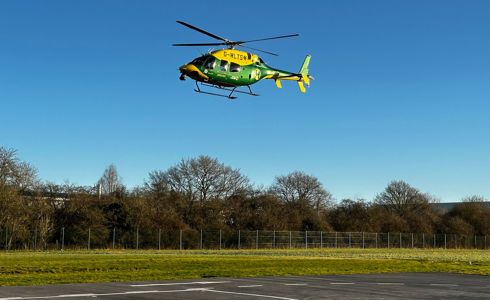 A yellow and green helicopter taking off from a helipad in blue skies