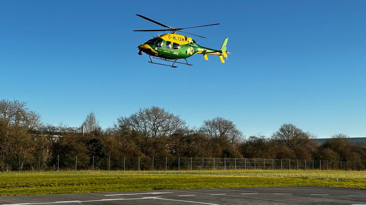 A yellow and green helicopter taking off from a helipad in blue skies