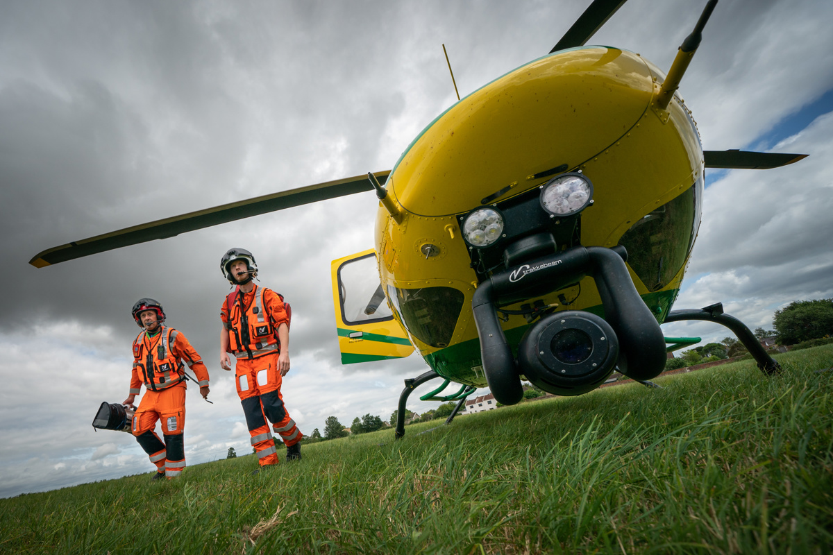 The nose of a yellow and green aircraft with two paramedics wearing orange flight suits walking alongside