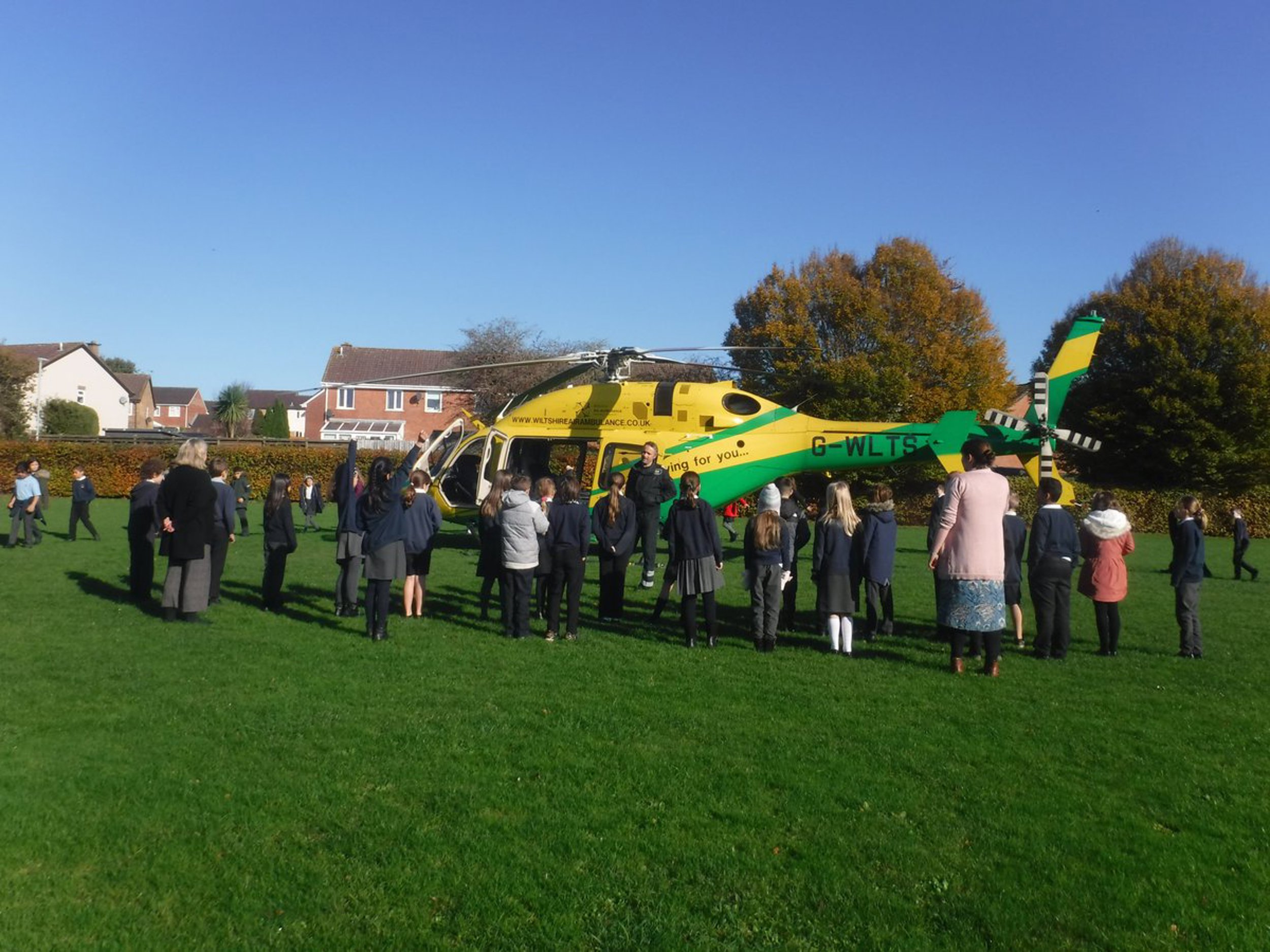 A yellow and green Wiltshire Air Ambulance helicopter surrounded by children