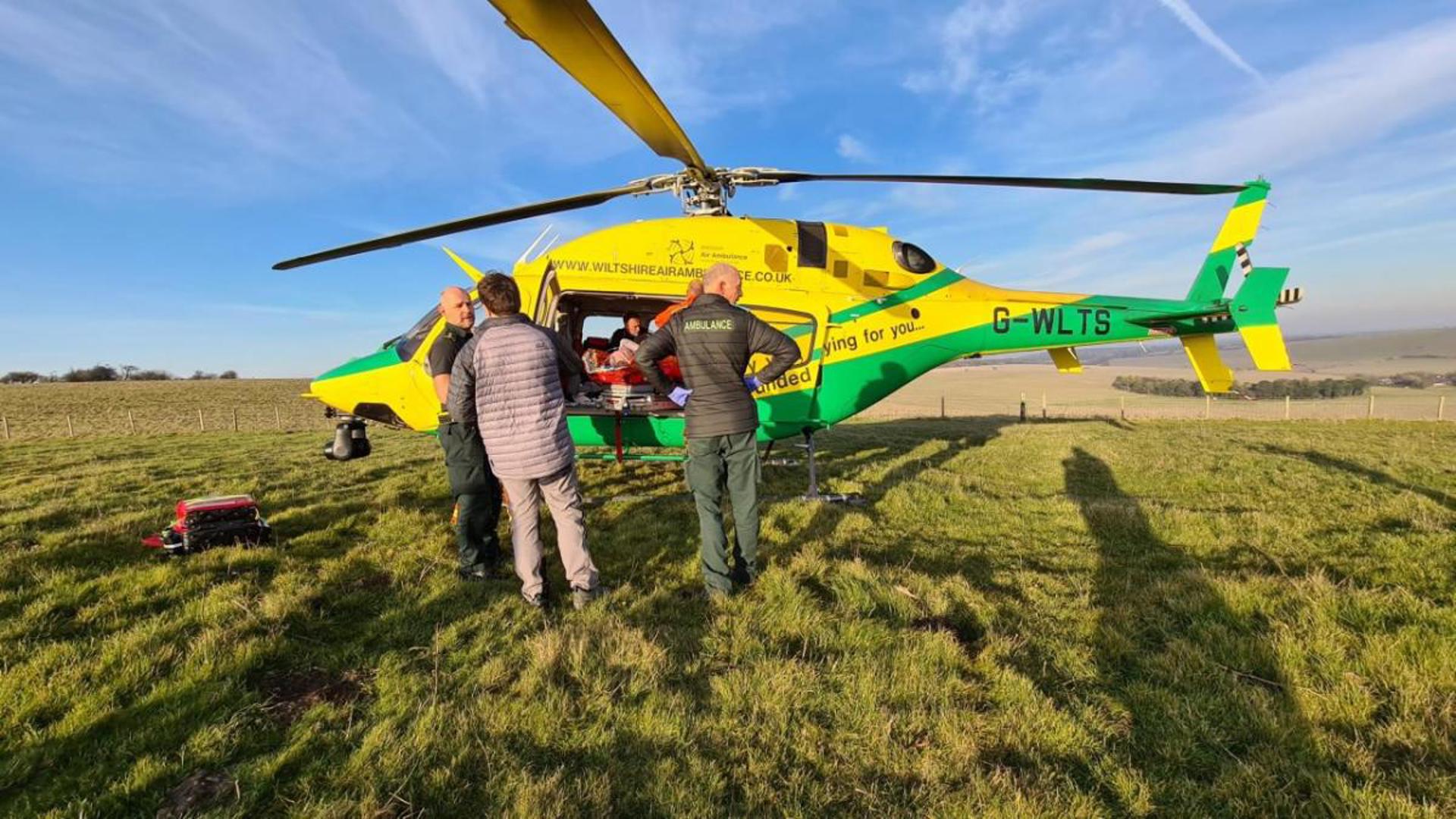 Wiltshire Air Ambulance's helicopter in a field, loading a patient on board Wiltshire Air Ambulance's helicopter in a field, loading a patient on board