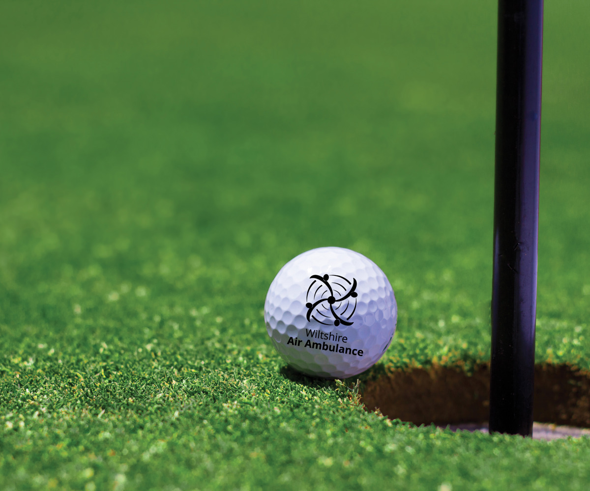 A Wiltshire Air Ambulance branded golf ball on the edge of a golf hole