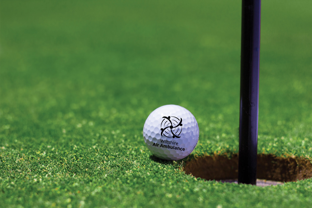 A Wiltshire Air Ambulance branded golf ball on the edge of a golf hole