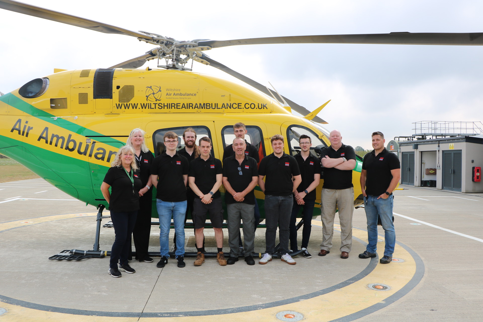 A group from Westek having their photo taken with a yellow and green helicopter A group from Westek having their photo taken with a yellow and green helicopter
