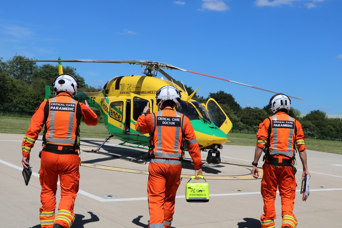 Two critical care paramedics, either side of a critical care doctor, walking towards a yellow and green helicopter